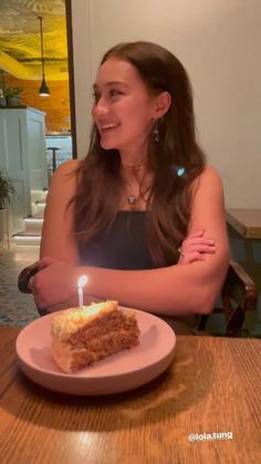 a woman sitting at a table in front of a piece of cake with a candle on it