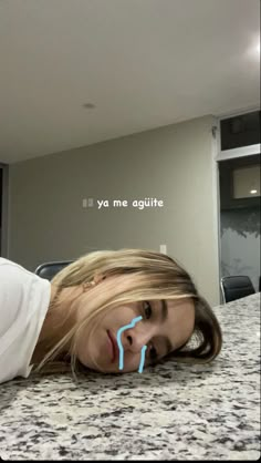 a woman laying on top of a kitchen counter next to a blue toothbrush in her mouth