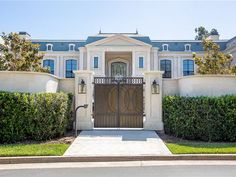 a large white house with blue shutters on the front and side doors, surrounded by hedges