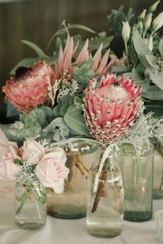 pink flowers are in vases on a white table cloth with candles and greenery