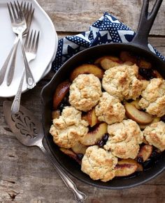 a skillet filled with food next to silverware and utensils on top of a wooden table