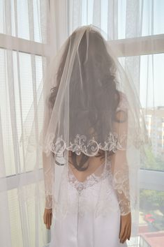 the back of a woman's head wearing a veil and wedding dress in front of a window