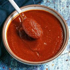 a bowl filled with red sauce and a wooden spoon in it on a blue table cloth