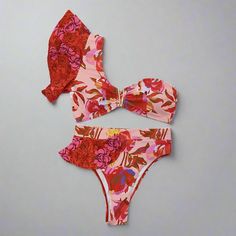 Step into paradise with our Tropical Bloom One-Shoulder Bikini Set. This eye-catching bikini features a vibrant floral print in shades of red, pink, and orange, evoking the beauty of a tropical garden. The one-shoulder top is designed with a stylish ruffle detail, adding a touch of femininity and flair, while the high-waisted bottoms offer a flattering and comfortable fit. Crafted from high-quality polyester and spandex, this bikini set ensures durability and comfort. The quick-drying fabric kee Beachwear Swimwear, Off-shoulder, Off-shoulder Beachwear Swimwear, Off-shoulder Swimwear For Sunbathing Beach Season, Red Tropical Printed Swimwear, Red Tropical Print Swimwear For Vacation, Floral Print Swimwear For Vacation Party, Pink One-shoulder Beachwear Swimwear, Pink One-shoulder Swimwear, Red Tropical Print Swimwear For Summer