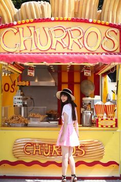 a woman standing in front of a food stand that sells churros and french fries