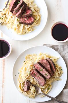 two white plates topped with meat and noodles next to cups of wine on a table