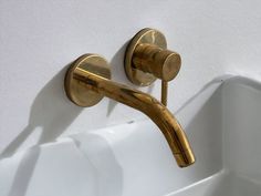 a gold faucet on the side of a white wall next to a sink