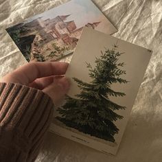 a person holding up some cards with trees on them in front of a bed sheet