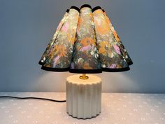 a lamp that is sitting on top of a table with a flowered shade over it