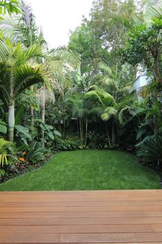 a wooden deck in the middle of a lush green garden with lots of trees and plants