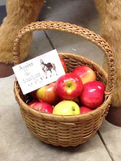 a basket full of apples sitting on the ground next to a stuffed animal's legs