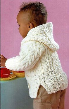 a small child wearing a white knitted sweater and holding a plate with food on it