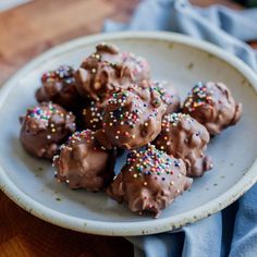 a white plate filled with chocolate covered donuts on top of a wooden table next to a blue napkin