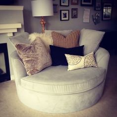 a white chair with pillows on it in front of a fire place and pictures on the wall