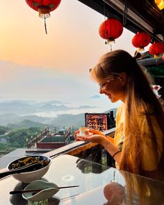 a woman looking at her cell phone while sitting at a table with food on it