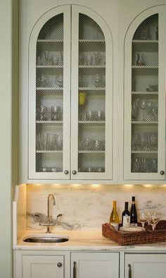 a kitchen with white cabinets and wine glasses on the counter top, along with two bottles of wine