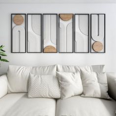 a living room with white couches and three framed art pieces on the wall above them