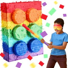 a young boy holding a stick in front of a rainbow colored box with circles on it