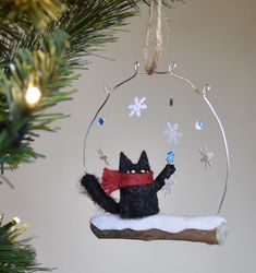 a black cat ornament hanging from a christmas tree with snowflakes on it