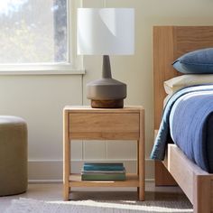 a bedroom with a bed, nightstand and lamp on it's night stand in front of a window