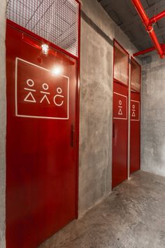 three red doors with symbols on them in a concrete wall and floored area next to each other