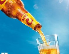 a beer being poured into a glass in front of a blue sky with the sun shining on it