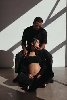 a man standing next to a pregnant woman on the floor in front of a white wall