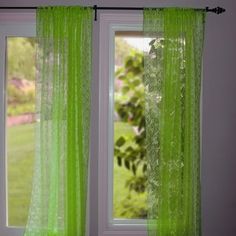 green curtains are hanging in front of a window with the view of a garden outside