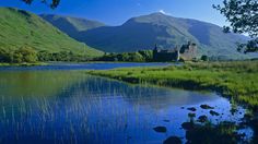 a castle sitting on top of a lush green hillside next to a lake with ducks swimming in it