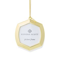 a gold and white ornament hanging from a chain on a white background with the words, kendra scott picture frame