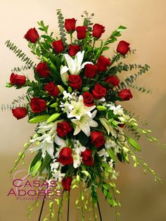 a bouquet of roses and lilies arranged on a stand in front of a wall