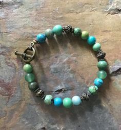 I think you will love the green and blue colors in this pretty turquoise and jade bracelet.  It is made with turquoise, jade, and turquoise howlite. The mixture of greens and blues are beautiful together. The antiqued brass accents give it a vintage look. It can be worn with any color of clothing, and it is a great addition to you bracelet collection and you will probably chose to wear it often. 8 1/2 inches long Bohemian Beaded Bracelets In Turquoise Chrysocolla, Green Agate Hand-strung Bracelets, Hand-strung Green Agate Bracelets, Green Agate Beaded Bracelets With Gemstones, Green Agate Beaded Bracelets With Gemstone Beads, Hand-strung Turquoise Jade Bracelets, Green Agate Gemstone Beaded Bracelets, Turquoise Chrysocolla Bracelet, Turquoise Agate Bohemian Bracelets