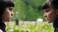 two young women standing next to each other in front of a green field and trees