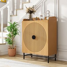 a wooden cabinet sitting next to a plant in a room with white walls and stairs