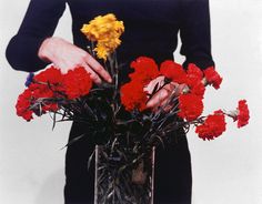 a woman holding a vase filled with red and yellow carnations in her hands