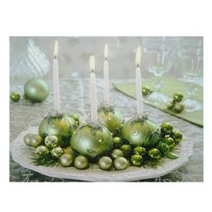 a table topped with green ornaments and lit candles in front of a plate filled with balls