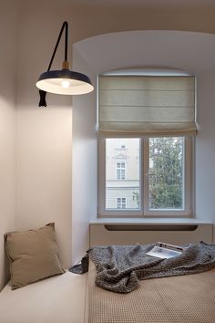 a bed sitting under a window next to a lamp and a blanket on top of it