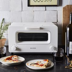 two slices of pizza sitting on plates in front of a toaster oven and bottle of wine