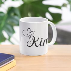 a white coffee mug sitting on top of a wooden table next to a book and plant