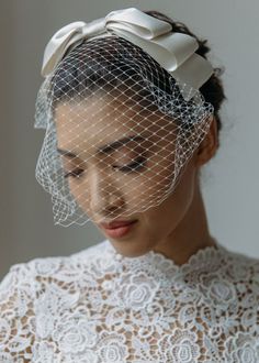 a woman wearing a white veil with a bow on it's head is looking down at her face