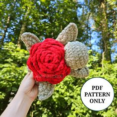 a hand holding up a crocheted stuffed animal with a red rose on it