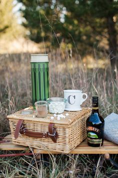 a picnic basket with coffee, hot chocolate and marshmallows sits on the ground