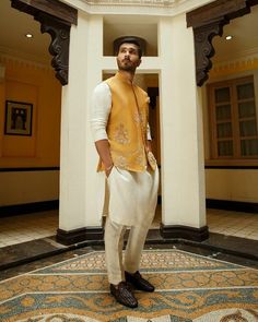 a man standing in front of a doorway wearing a yellow vest and white pants with black shoes