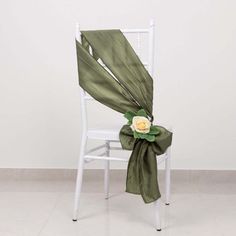 a white chair with a green sash and flower on it's back, sitting in front of a wall