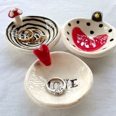 three ceramic bowls with rings in them on a white tableclothed surface, one has a ring holder and the other has a wedding band