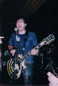 a man singing into a microphone while holding a guitar in front of two other people