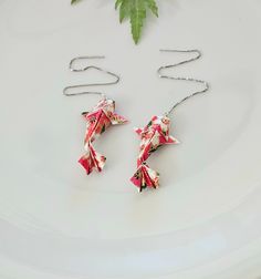 two pink origami stars are hanging from a chain on a white plate next to a green plant