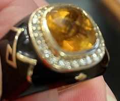 a close up of a person's hand holding a ring with an orange stone