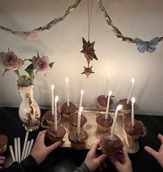 two hands reaching for cupcakes on a tray with lit candles in front of them