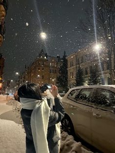 a woman standing on the side of a snow covered road taking a photo with her cell phone